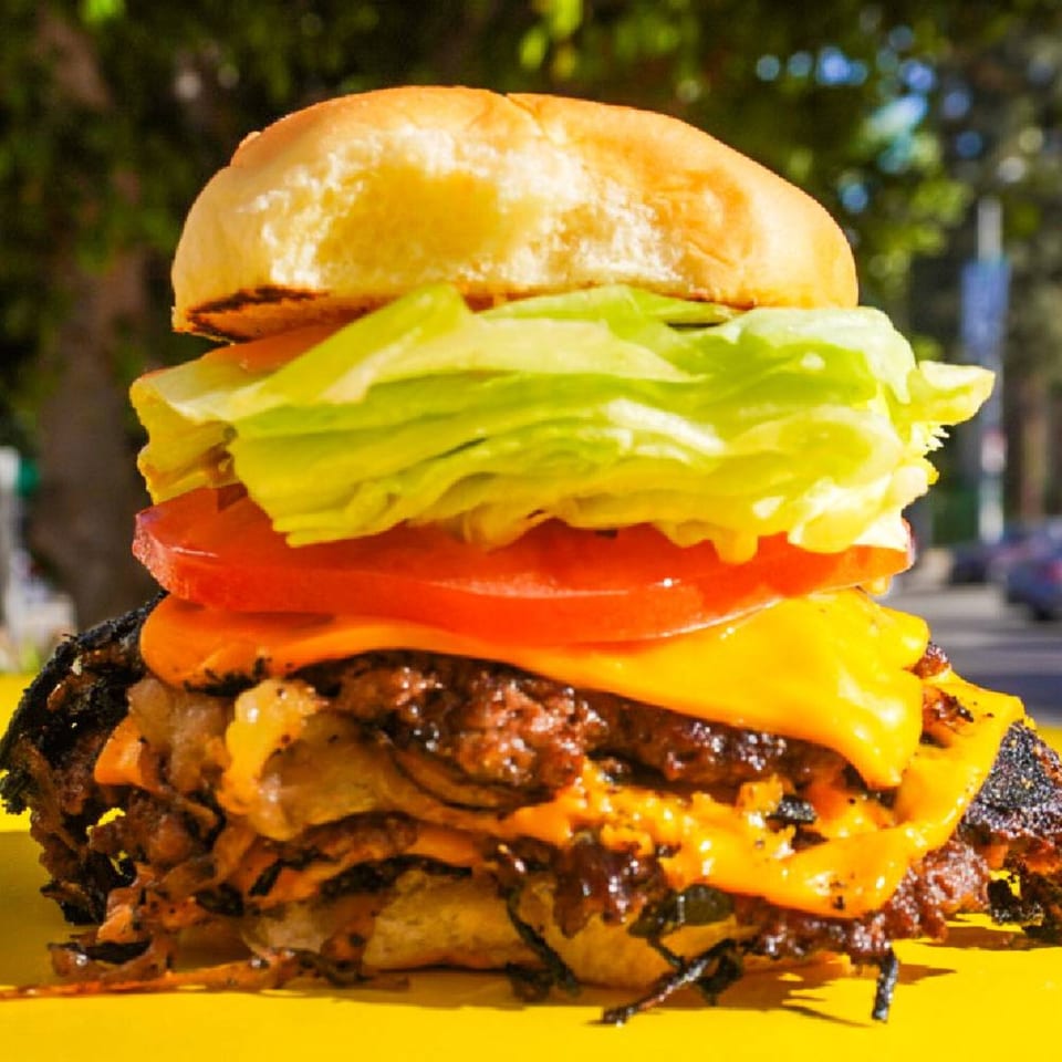 A Patty Smash Brand burger with two patties, melted cheese, lettuce, and tomato on a yellow surface.