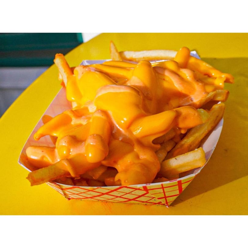 Crispy golden fries generously topped with melted orange cheese sauce in a paper tray.