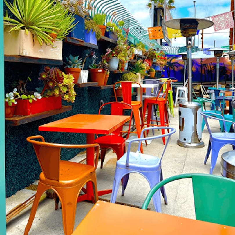 Vibrant outdoor patio with colorful tables and chairs, lush plants, and festive string lights.