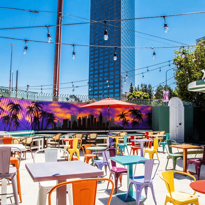 Patty Smash Brand's vibrant outdoor patio with colorful tables and chairs, a mural, and string lights.